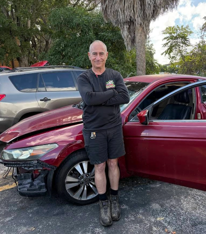 A man standing proudly next to a damaged red Honda Accord, representing who buys wrecked cars in Fort Lauderdale.