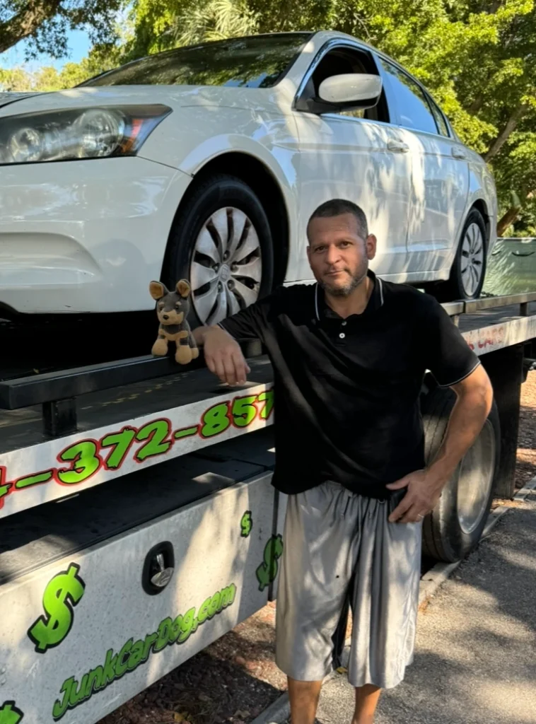 Man standing next to a flatbed truck hauling a white sedan, representing cash for junk car in Cooper City.