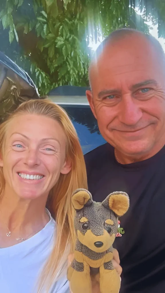 A woman in a white t-shirt and a man in a black shirt holding a stuffed toy dog beside a car, promoting Cash for Junk Car in Boca del Mar.