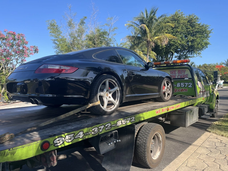 Black sports car on a green tow truck representing Junk Car Buyers in Fort Lauderdale