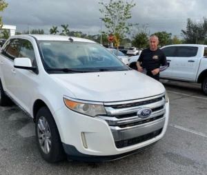 White Ford SUV parked in a parking lot with a person standing next to it promoting cash for junk car Tamarac