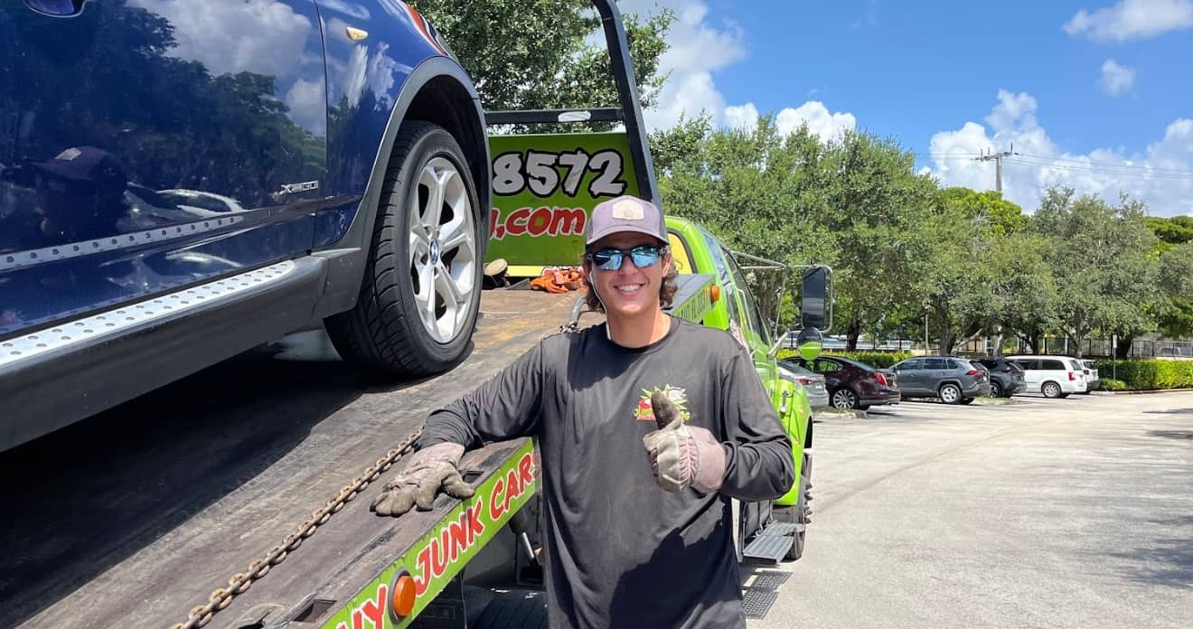 Person giving a thumbs-up beside a tow truck carrying an SUV, representing a successful junk car sale for Flooded Cars in Miami.