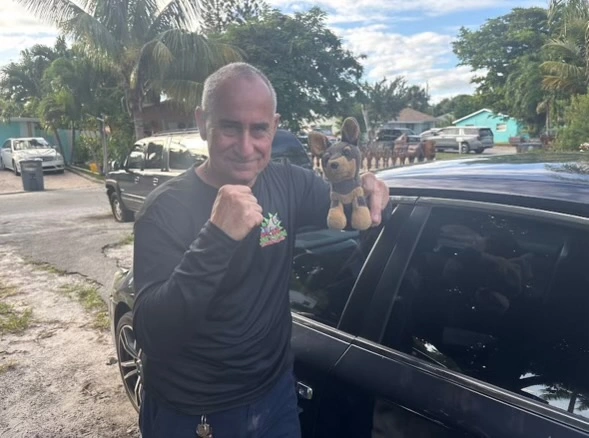 A junk car buyer in Coral Springs FL holds a stuffed toy while standing beside a car