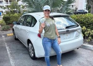 Person holding dollar bills in a parking lot beside a Junk Cars Hialeah