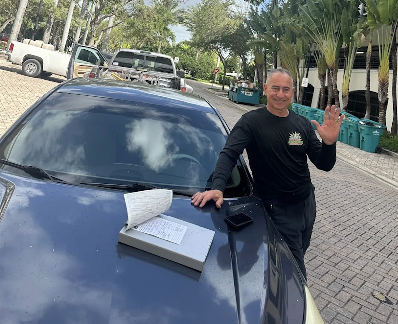 A professional junk car removal Fort Lauderdale specialist standing next to a vehicle with paperwork.