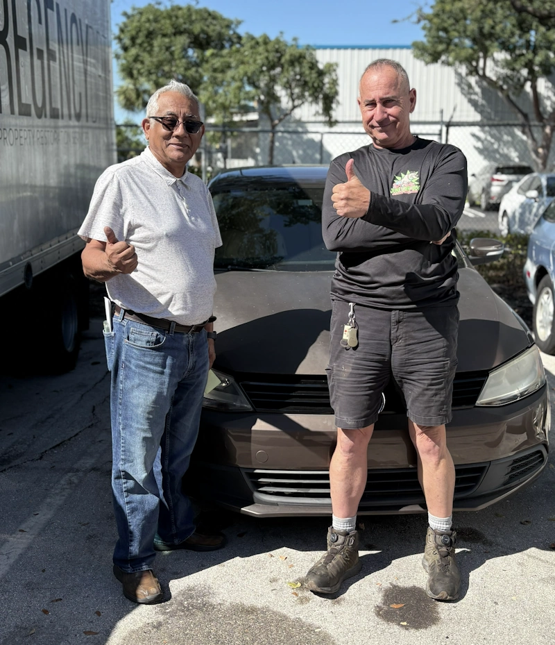 Two men giving a thumbs up in front of a brown sedan, representing a Junk Car Dog we buy junk cars in Lauderhill service.