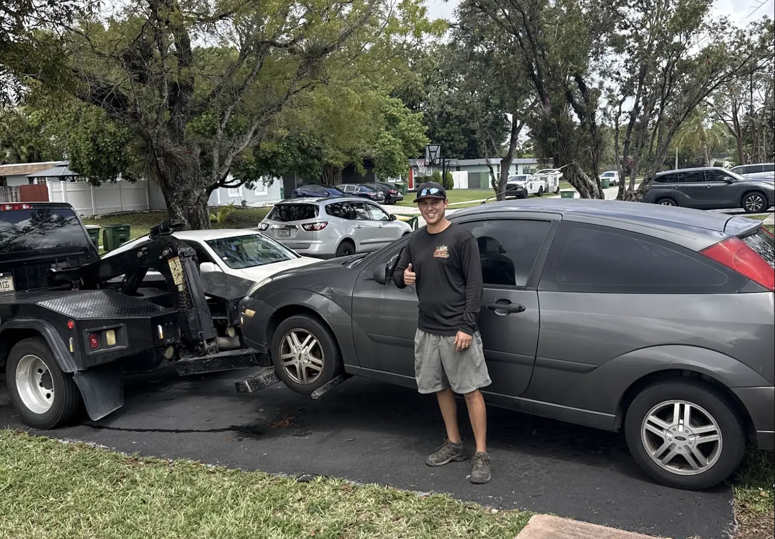 A man gives a thumbs-up next to a sedan being loaded onto a tow truck, representing same day junk car pick up in Tamarac.