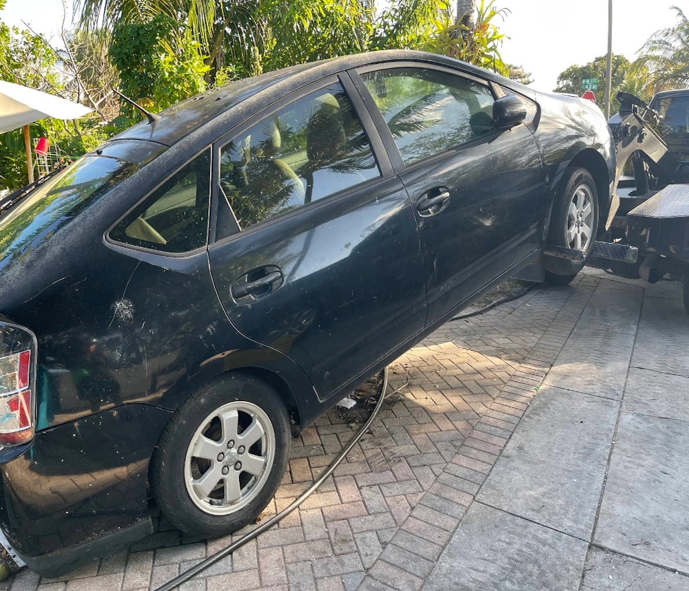 An old Toyota Prius being lifted onto a tow truck for removal.