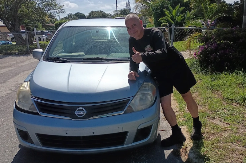A man giving a thumbs-up while leaning against a sedan, illustrating how to stay protected against common junk car buyer scams.