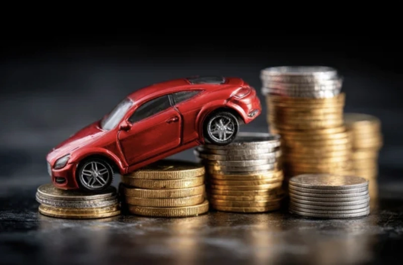 A small red toy car driving up stacks of gold and silver coins, conceptualizing how to maintain car value over time.