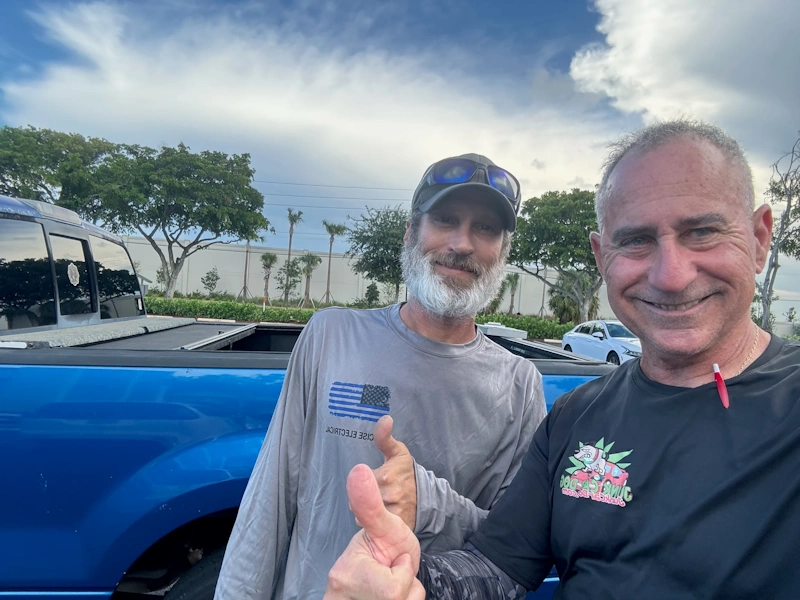 Two smiling men giving a thumbs-up in an outdoor parking lot, highlighting a hassle-free solution to the common problems with keeping junk cars.
