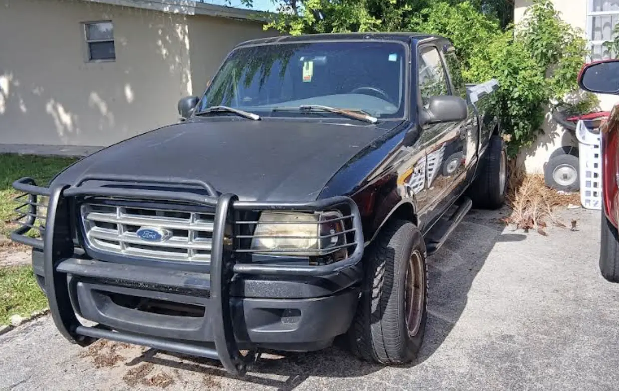 A black Ford Ranger with a front brush guard parked on a driveway, showing visible signs of aging and rust on the wheel rims.